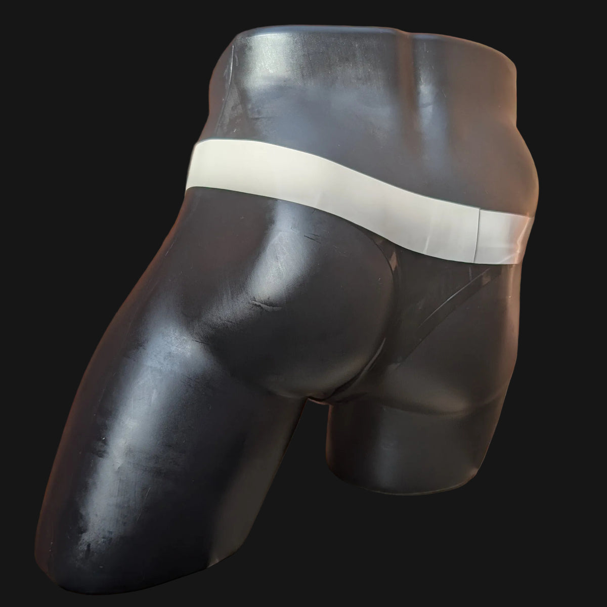A black male mannequin torso wearing a black thong-style underwear bottom with a wide white waistband